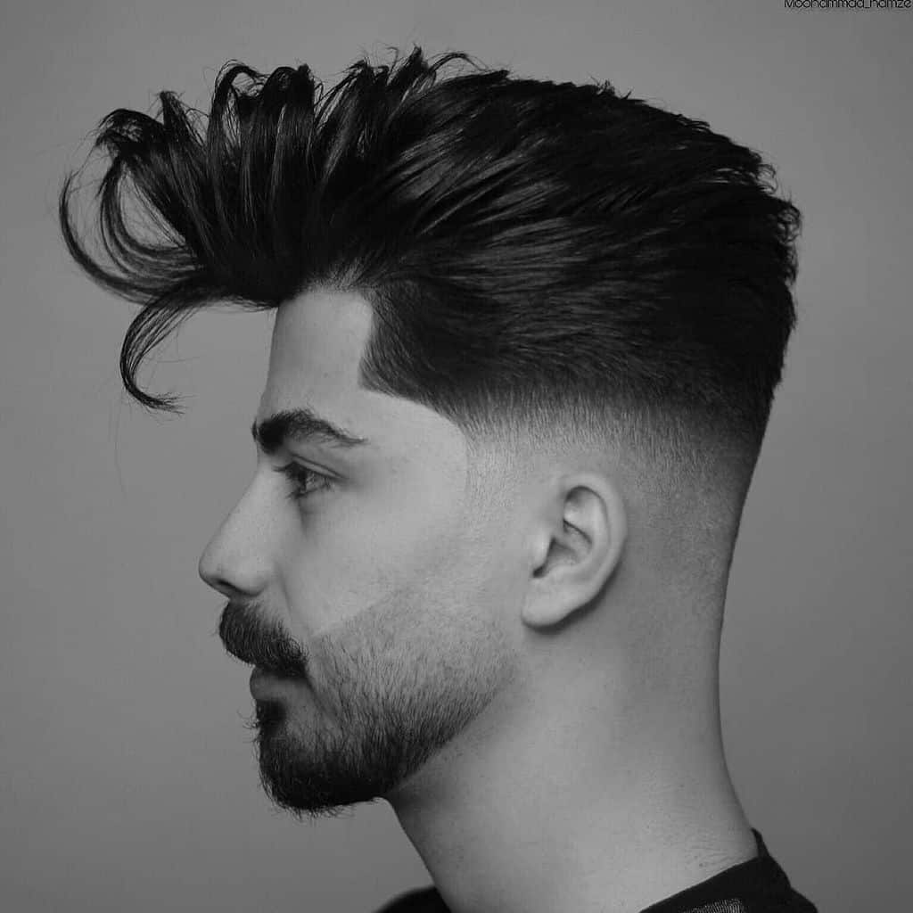 A blown out hair on top paired with mid faded sides and back with clean hairline extending to the beard