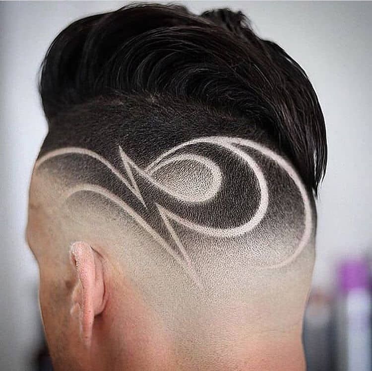 A mid-fade haircut with long textured hair on top and designs on the nape of the neck