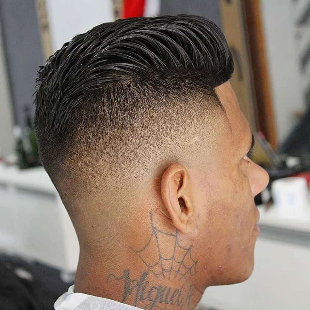 A pompadour with back combed hair paired with mid-faded sides and back with tattoo below the ear