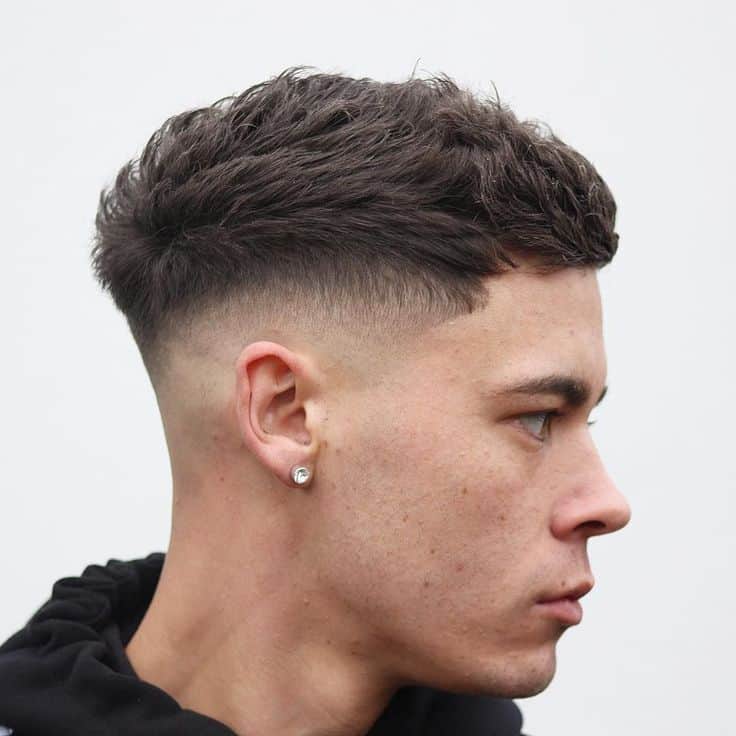 A forward combed quiff paired with a mid-fade